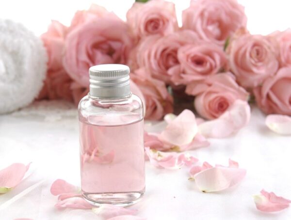 a bottle of liquid next to pink roses